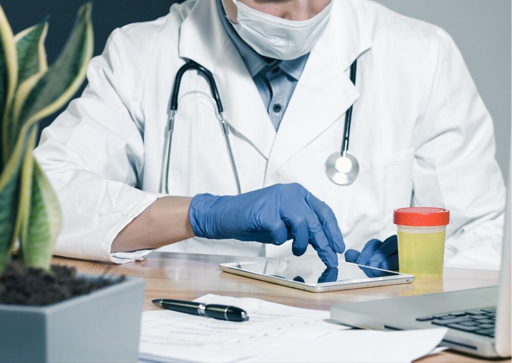 Lekarz siedzi przy biurku i bada stojący obok kubeczek z moczem pod względem obecności krwi w moczu.